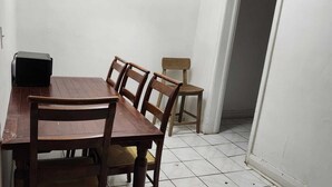 Un comedor con una mesa y sillas de madera, un altavoz negro y una pequeña mesa con una lámpara.