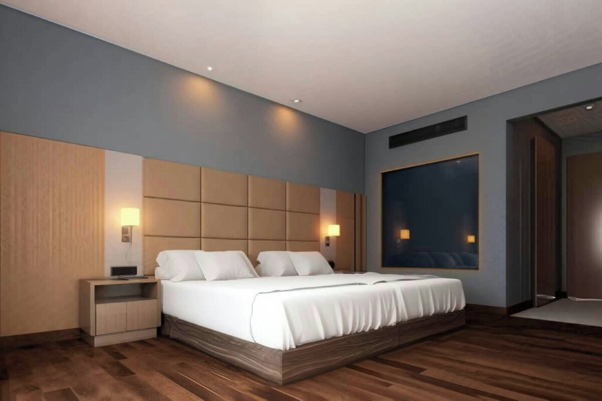 Une chambre d’hôtel moderne avec un grand lit, une tête de lit en bois, des lampes de chevet et une grande fenêtre.