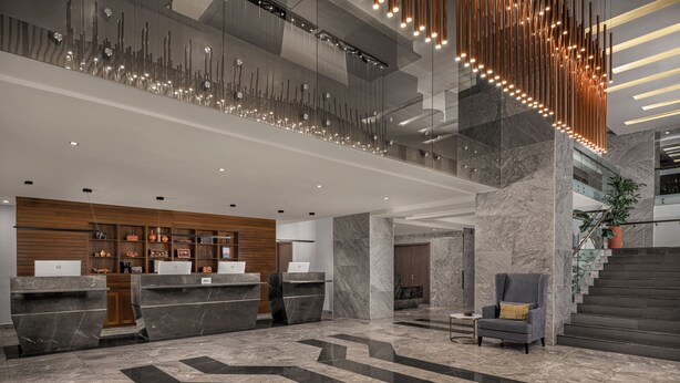 A modern hotel lobby with marble flooring, a reception desk, a staircase, and a contemporary light fixture. - Four Points® by Sheraton Accra Airport Hotel (Accra)