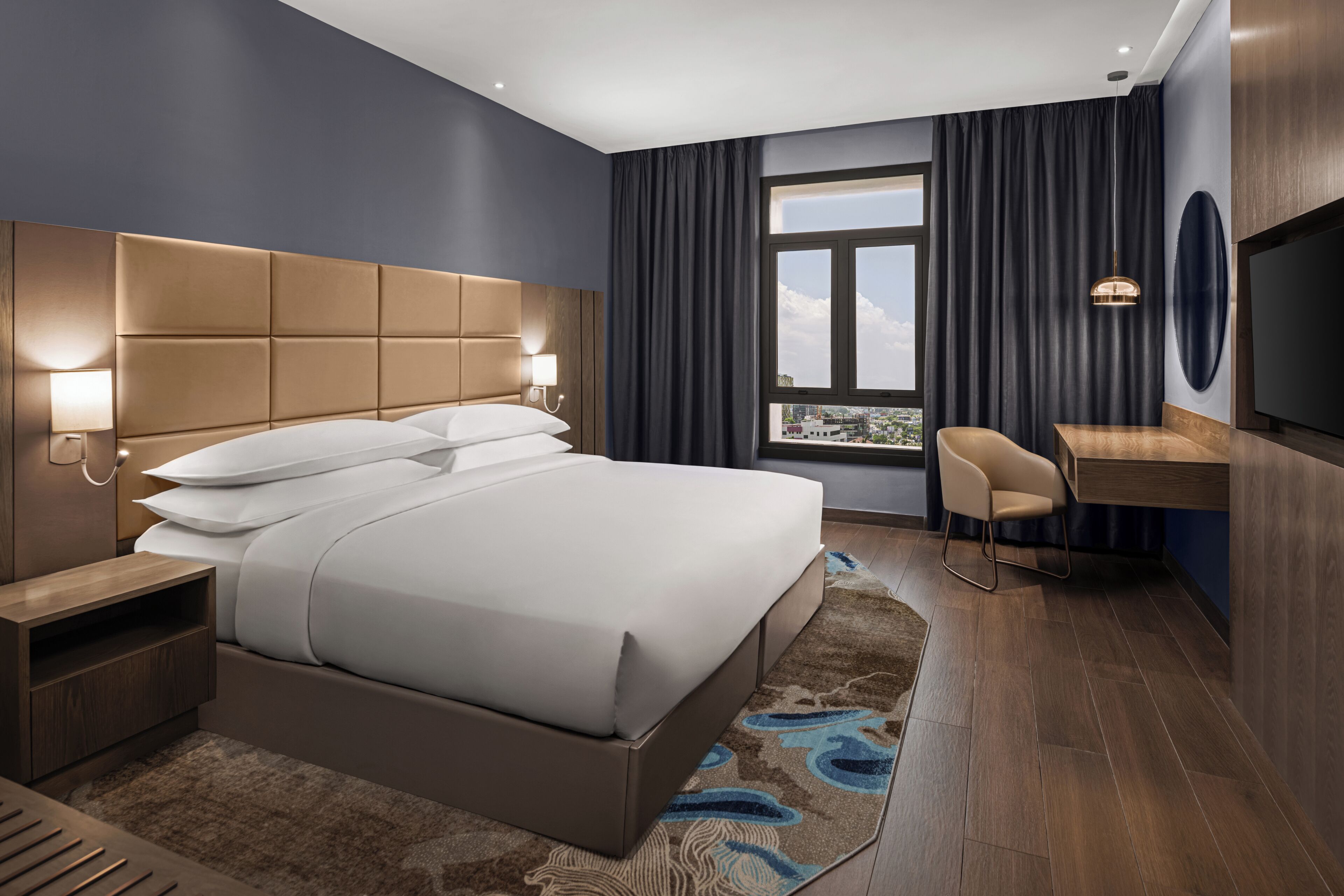 A modern hotel room with a large bed, bedside tables, a desk, and a TV.
