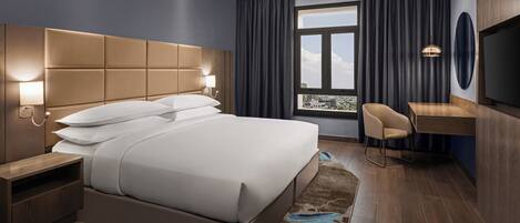 A modern hotel room with a large bed, bedside tables, a desk, and a TV.