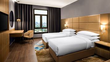A hotel room with a large bed, a desk, a chair, a TV, and a window with a city view.