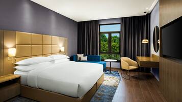 A hotel room with a large bed, a desk, a chair, a small table, and a TV.