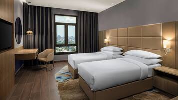 A hotel room with a large bed, a desk, a chair, and a view of the city through a window.