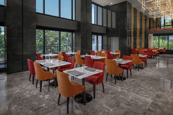 A spacious indoor dining area with multiple tables and chairs, large windows, and a modern chandelier. - Four Points® by Sheraton Accra Airport Hotel (Accra)