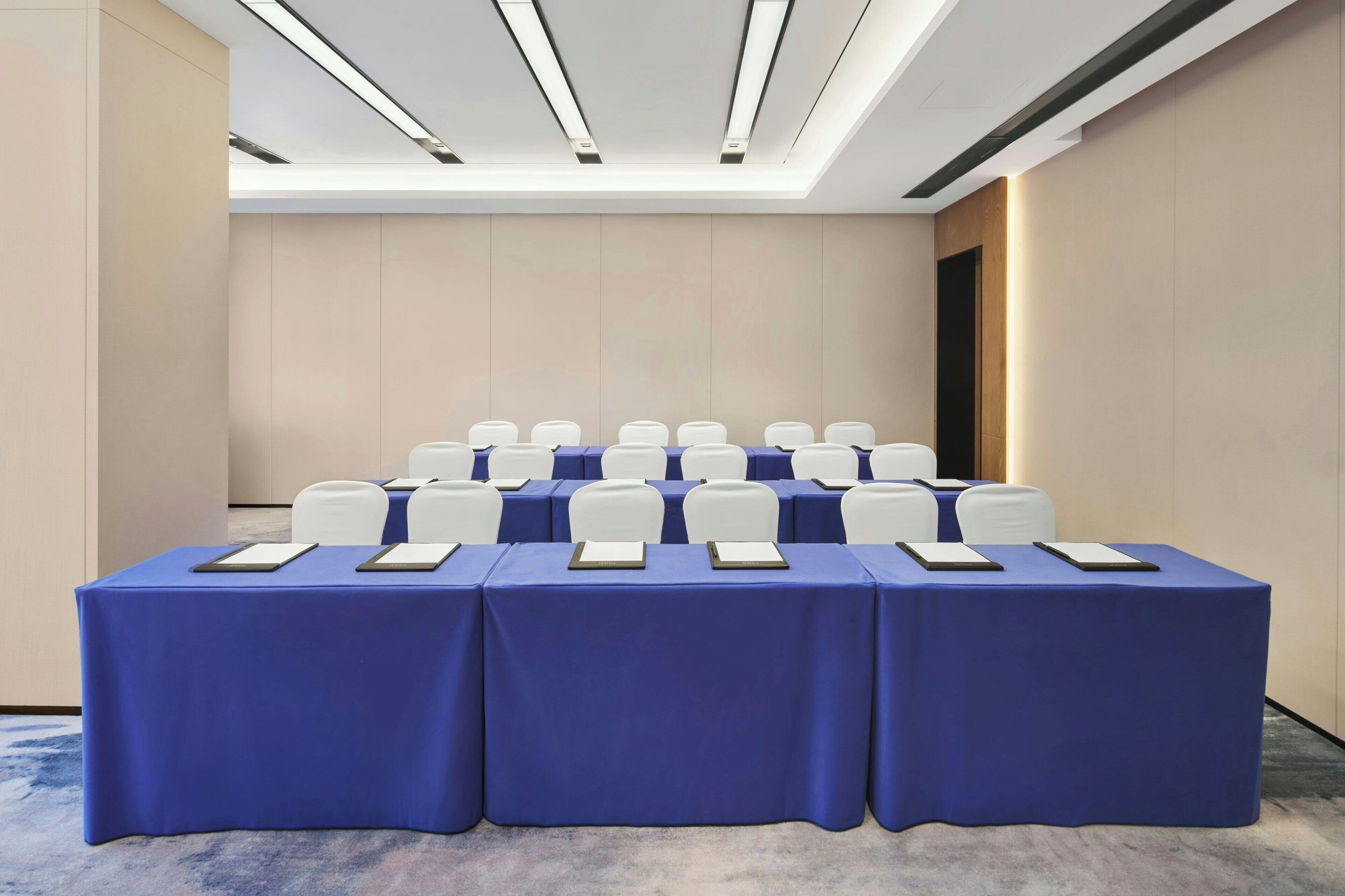 Une salle de conférence avec une nappe bleue, des chaises blanches et un plafond doté de luminaires linéaires.