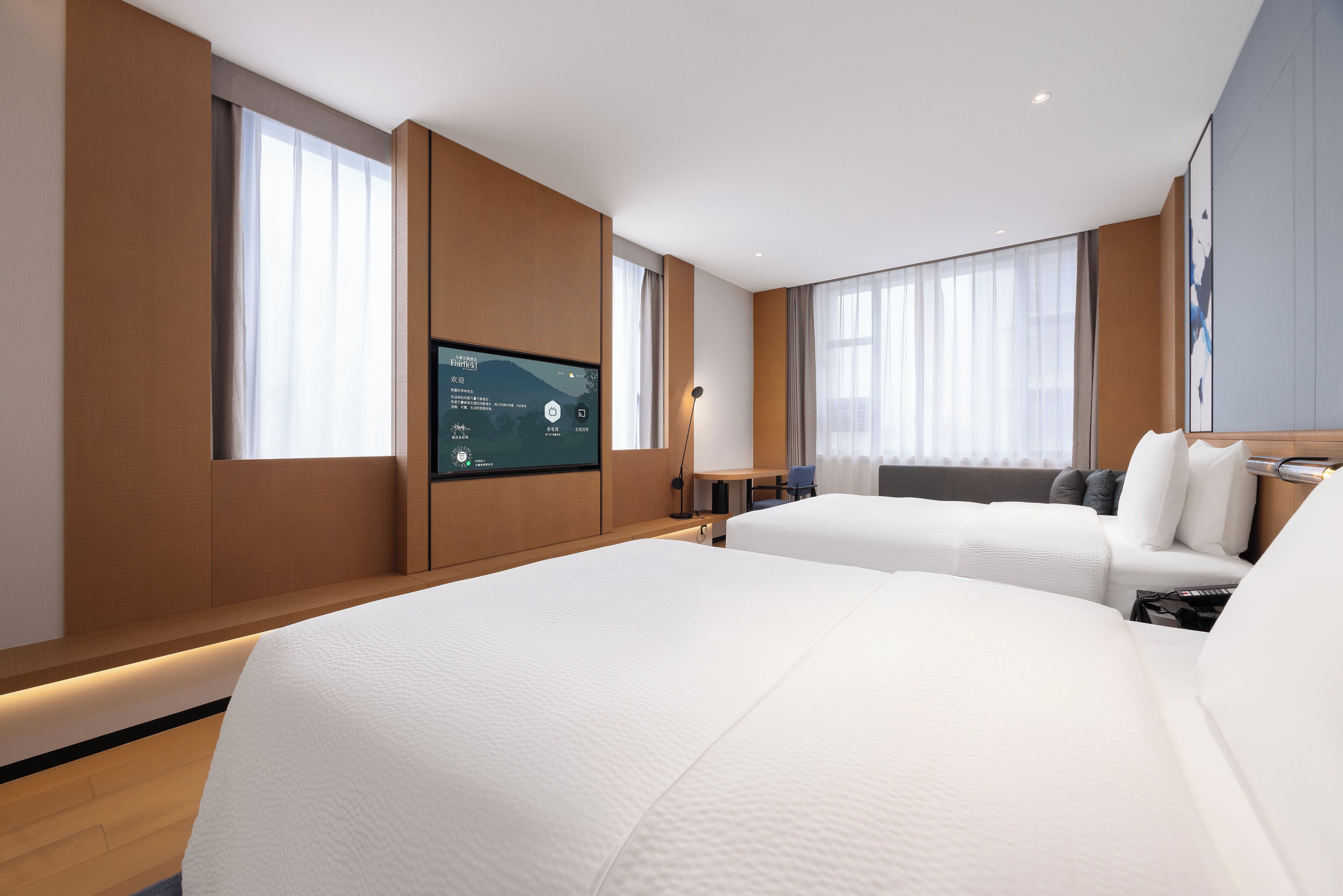 A modern hotel room with two beds, a flat-screen TV, and large windows.