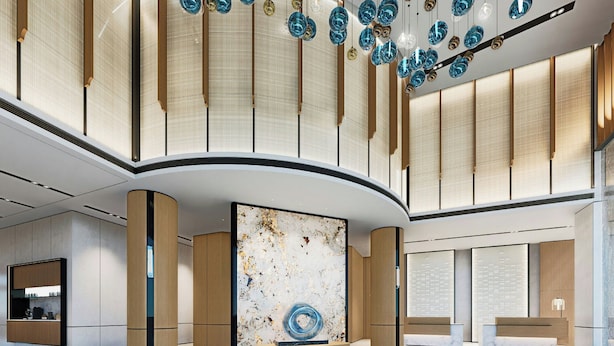 Un vestíbulo amplio con una instalación artística central, paneles de madera y luminarias modernas.