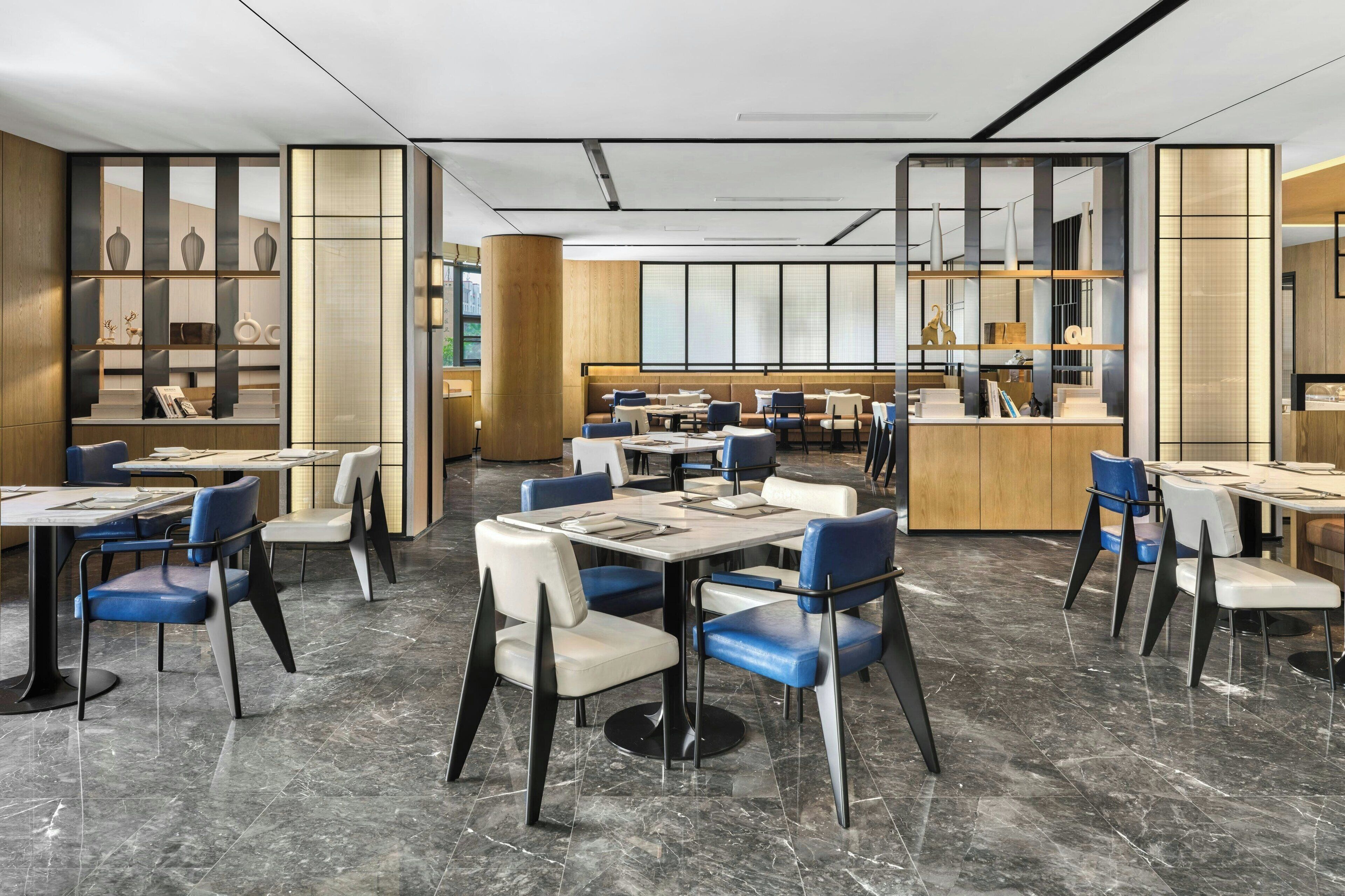 Een modern restaurant met marmeren vloeren, blauw-witte stoelen en houten details.