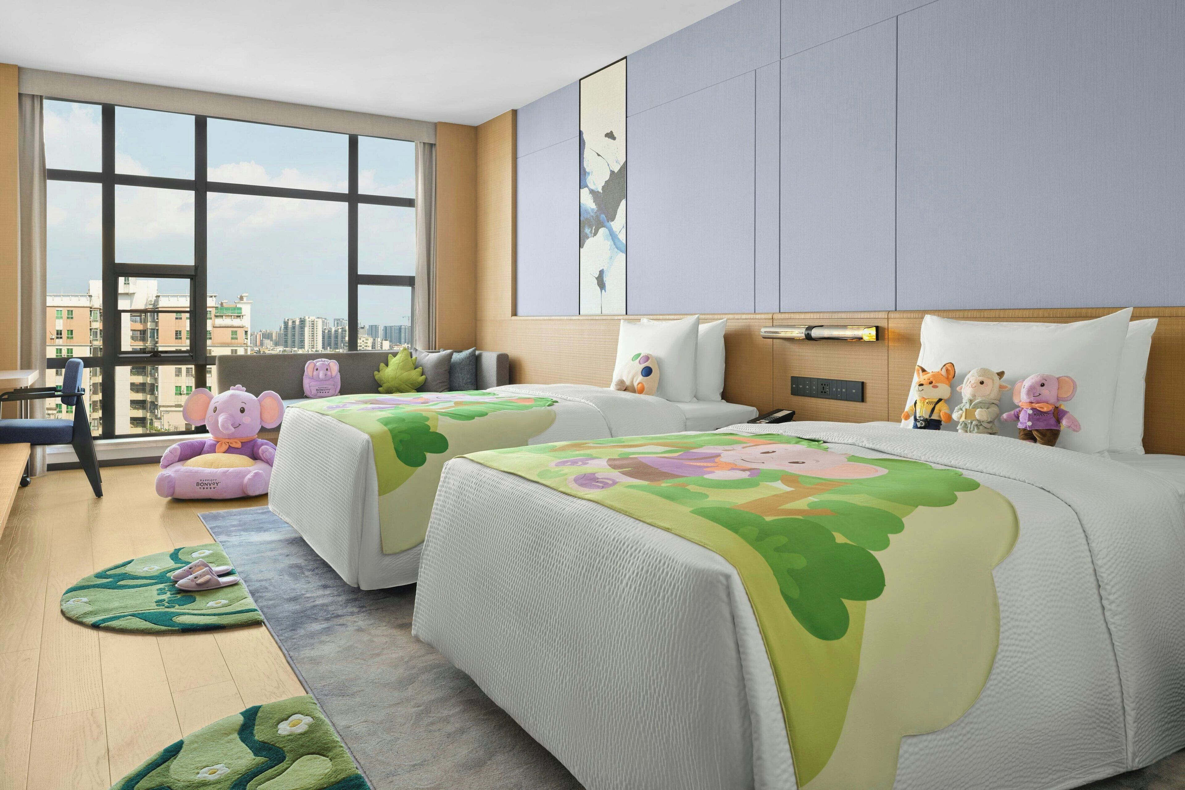 Habitación de hotel con dos camas, ventanas amplias, vista a la ciudad y peluches en las camas.
