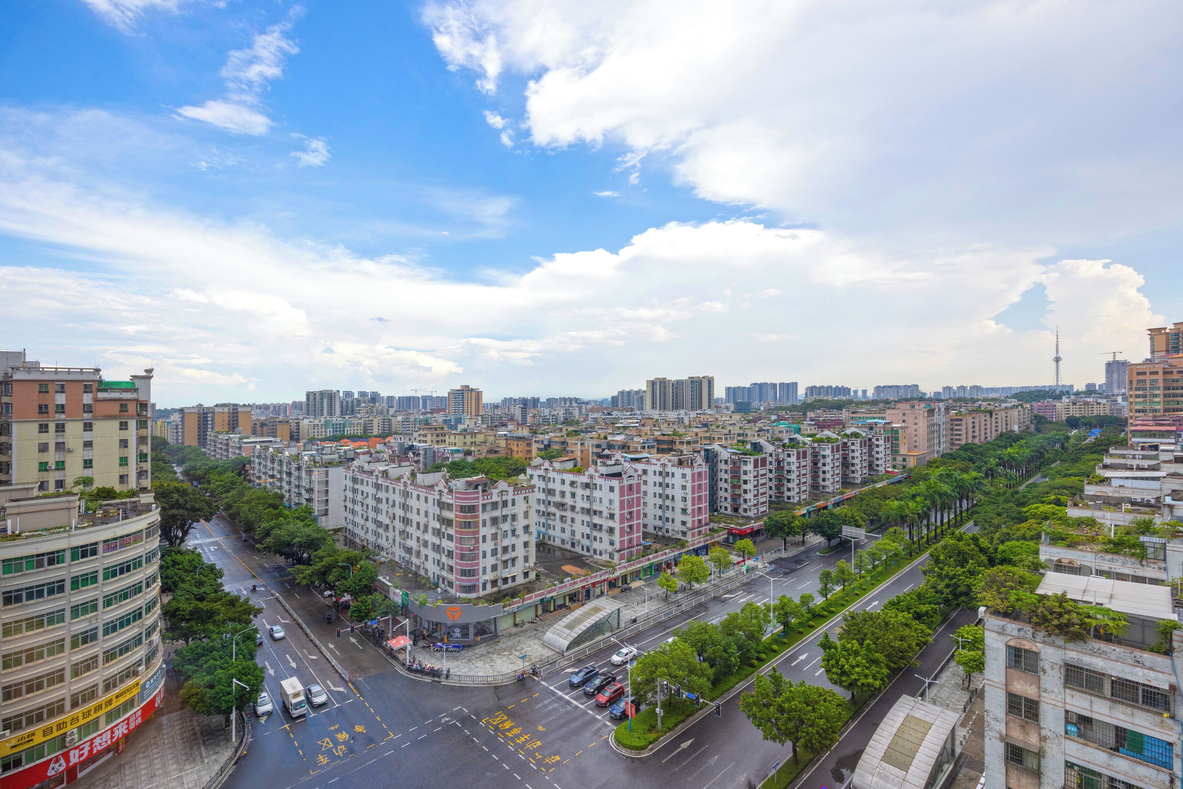 A cityscape with multi-story residential buildings, a wide road, and a clear sky.
