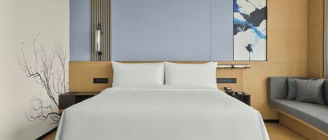 A modern hotel room with a large bed, a sofa, a wall-mounted artwork, and a minimalist design.