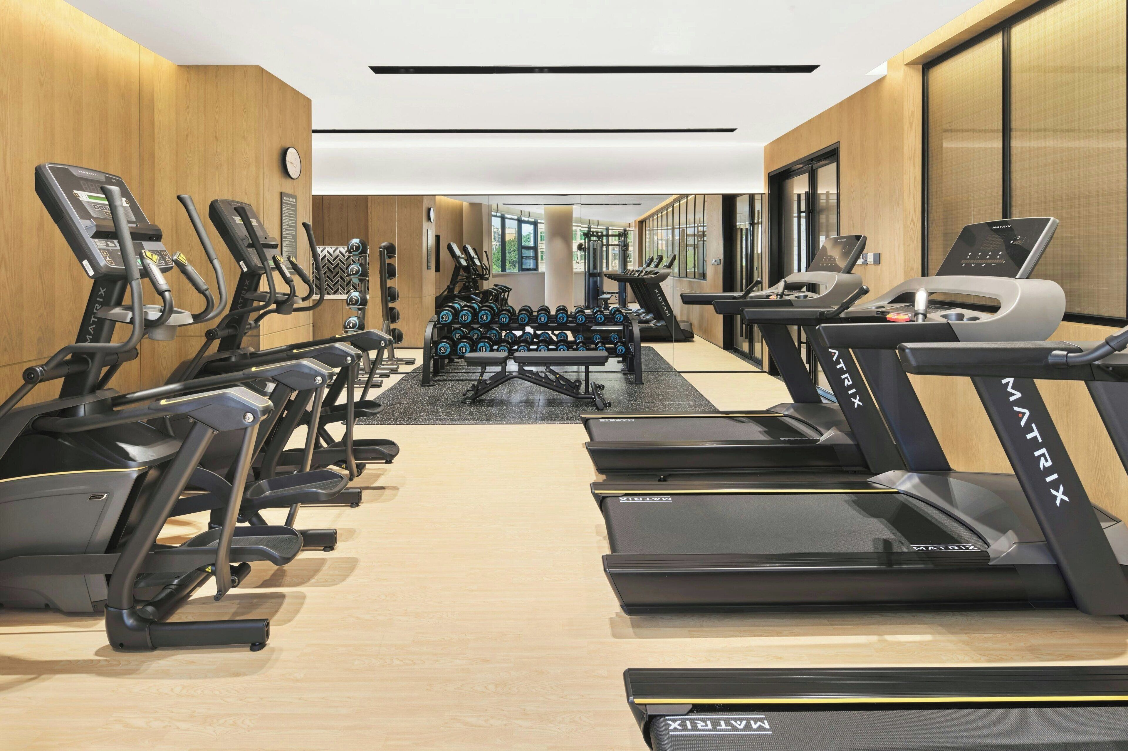 A gym with treadmills, elliptical machines, and dumbbells.