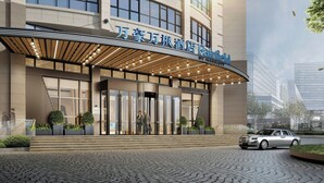 A hotel entrance with a modern design, featuring a covered entrance, large windows, and a paved driveway.