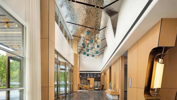 A modern lobby with a high ceiling, a chandelier, and a reception desk.
