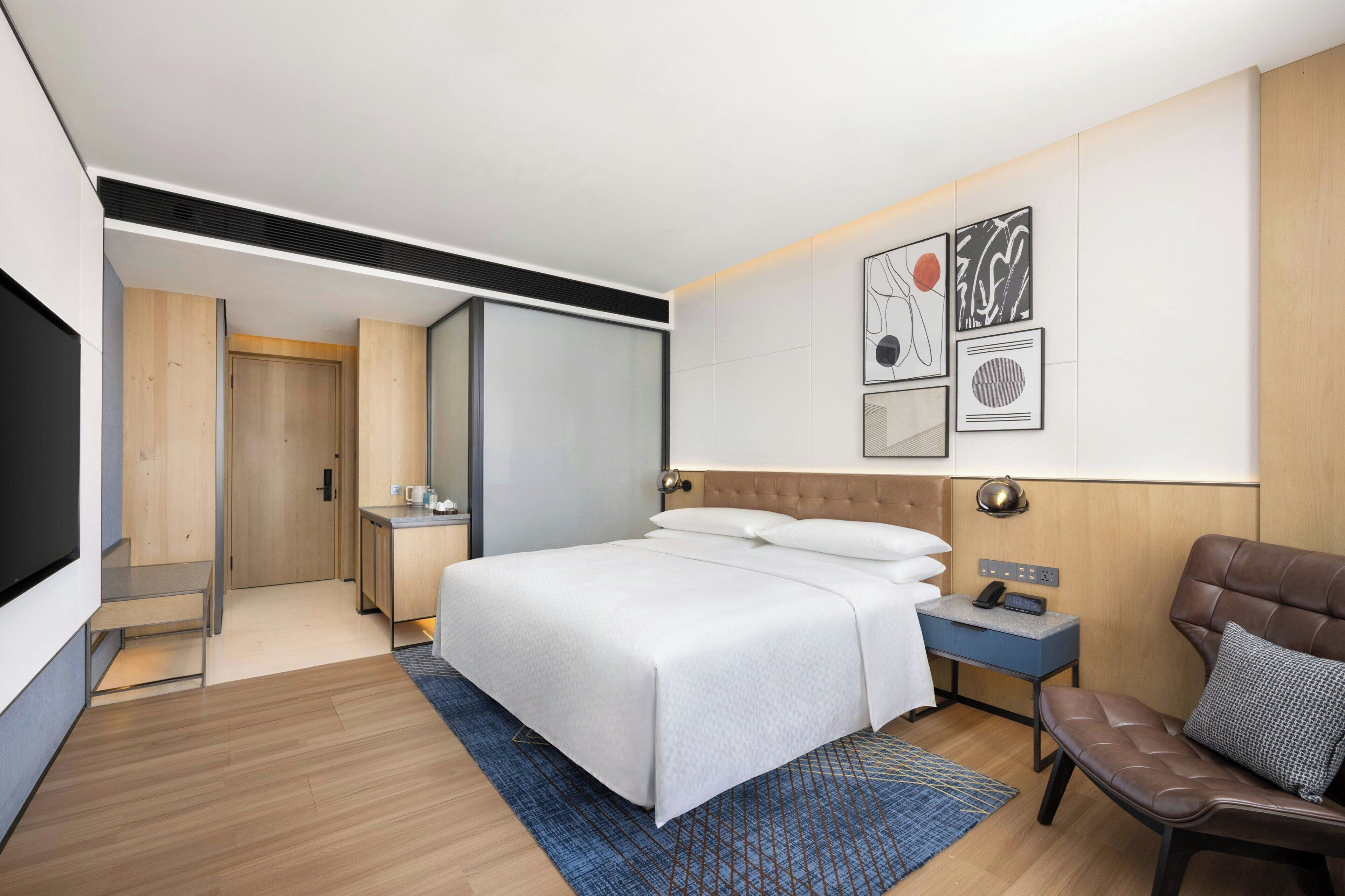Una habitación de hotel moderna con una cama grande, un escritorio, una silla y obras de arte en la pared.