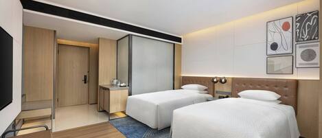 A hotel room with two beds, a desk, a chair, a wardrobe, and artwork on the wall.