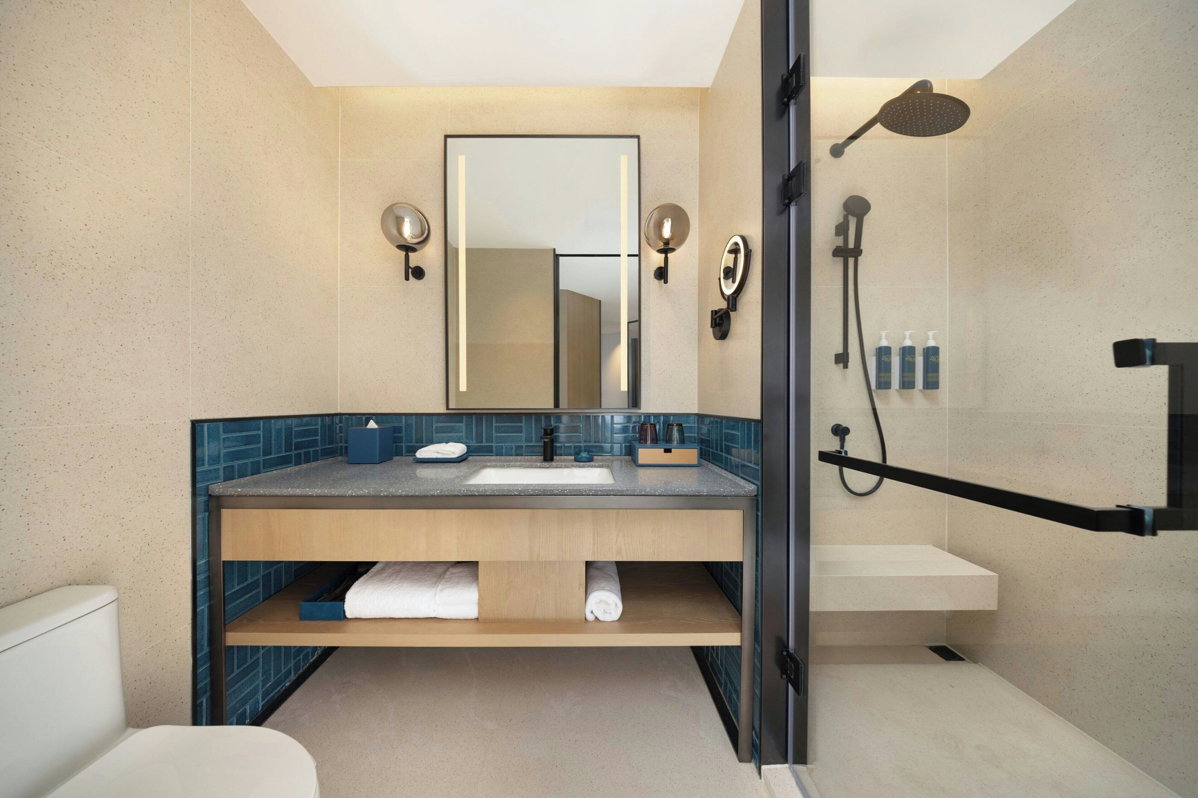 A modern bathroom with a large mirror, a shower, and a sink with a towel rack.