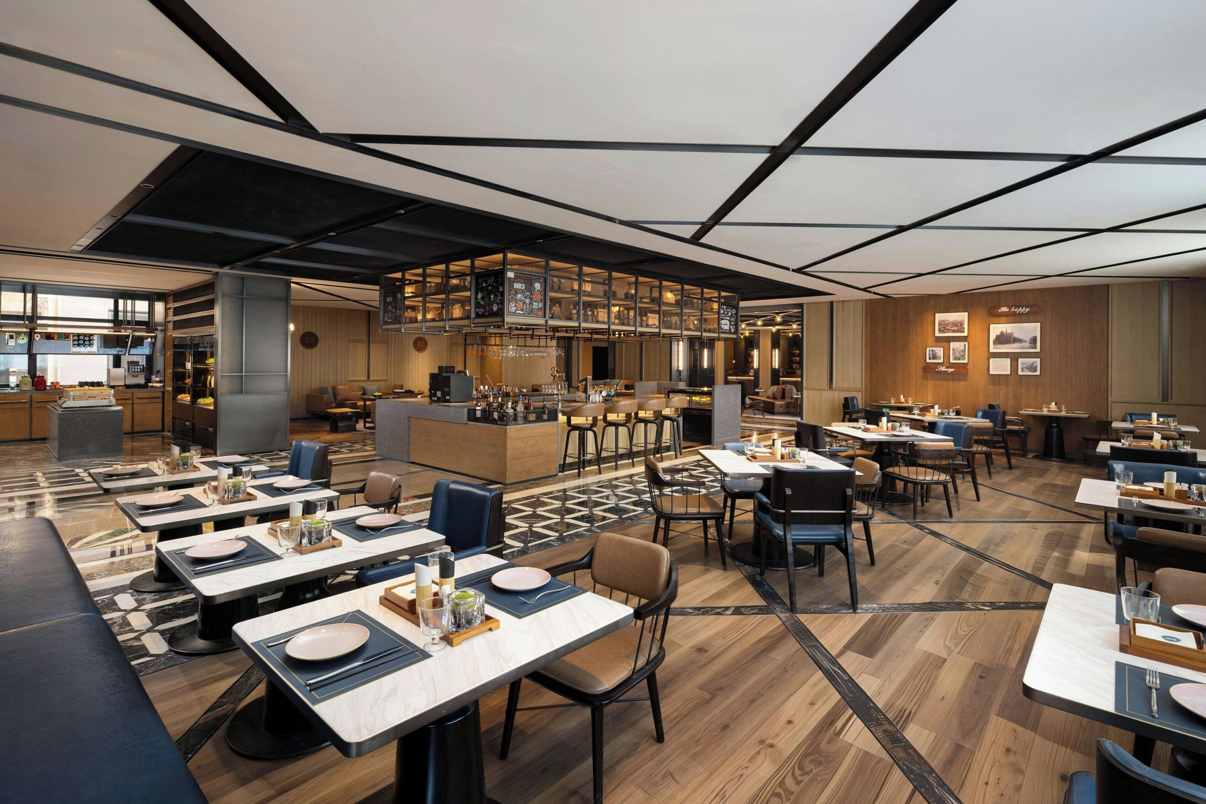 Ein modernes Restaurant mit mehreren Essbereichen, einer Bar und einer im Hintergrund sichtbaren Küche.