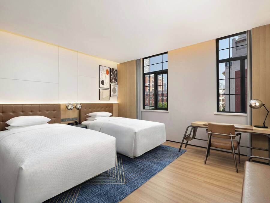 Quarto de hotel com duas camas, uma escrivaninha e uma cadeira.