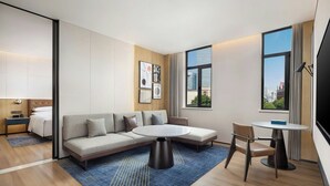 Ett modernt hotellrum med en soffa, ett litet bord, en stol, en säng och ett stort fönster med utsikt över staden.