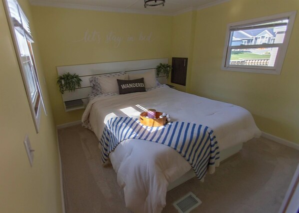 A bedroom with a bed, a bedside table, a window, and a wall with a sign.