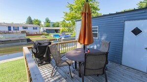 A deck with a table and chairs, a grill, and a covered umbrella. - Cozy 1-bedroom mobile home on the beautiful Crooked lake (Angola)