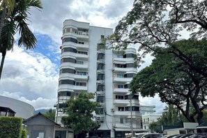 A multi-story residential building with balconies, surrounded by trees and parked cars.