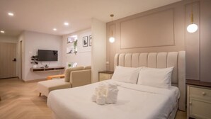 A modern hotel room with a large bed, a bedside table, a TV mounted on the wall, and a seating area with a sofa and chairs.