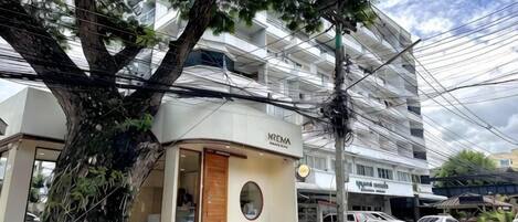 A hotel with a modern facade, a large tree in front, and a parking area with cars.