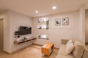 Ein modernes Wohnzimmer mit Flachbildfernseher, Couchtisch aus Holz und beiger Couch.