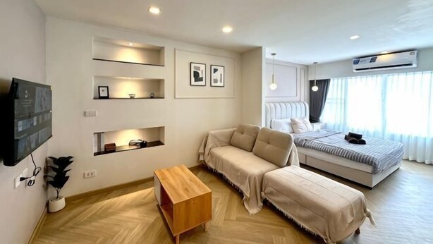 A modern bedroom with a bed, a sofa, a wooden coffee table, and built-in shelves.