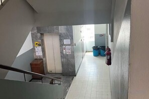 Un pasillo con pared de mármol, un extintor y un cubo de basura.