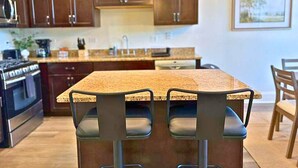 A kitchen with wooden cabinets, a granite countertop, and a central island with bar stools. - Well-Equipped 2BR - Greenbay 301 (Evanston)