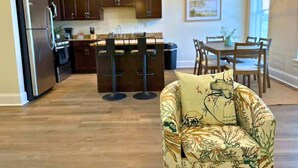 A modern kitchen with dark wooden cabinets, a stainless steel refrigerator, and a dining area with a table and chairs. - Well-Equipped 2BR - Greenbay 301 (Evanston)