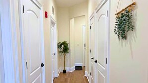 A hallway with white doors, a small plant, and a hanging decoration. - Well-Equipped 2BR - Greenbay 301 (Evanston)