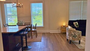 A spacious living area with a dining table and chairs, a sofa, and a small side table with a lamp. - Well-Equipped 2BR - Greenbay 301 (Evanston)
