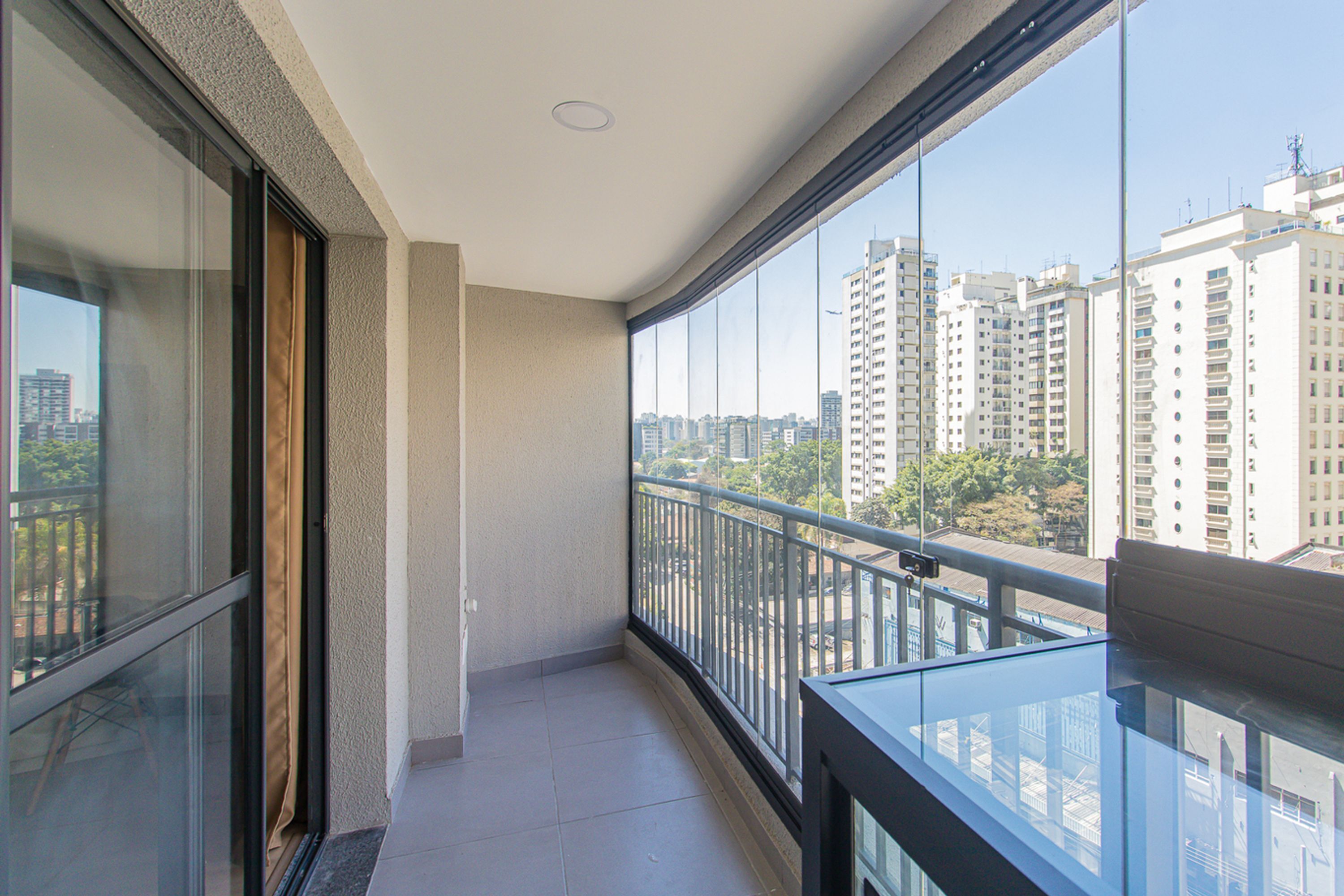A balcony with a glass railing, a view of high-rise buildings, and a tiled floor.