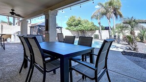 An outdoor patio with a table and chairs, a ceiling fan, and a view of a swimming pool and palm trees. - Fabulous 4-bedroom house with pool in Scottsdale (Scottsdale)
