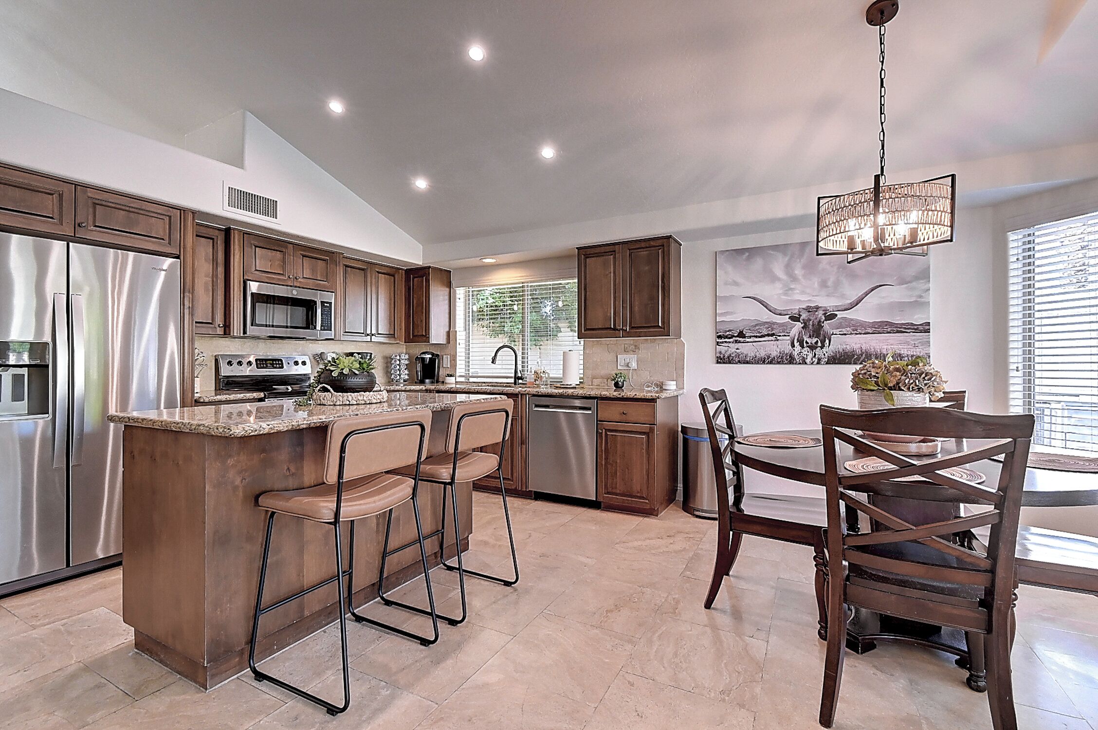 A modern kitchen with stainless steel appliances, a central island with bar stools, and a dining area with a chandelier.