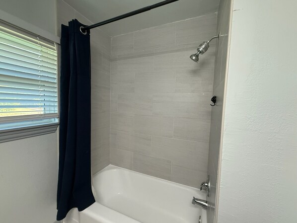 A bathroom with a bathtub, shower, and window with blinds.