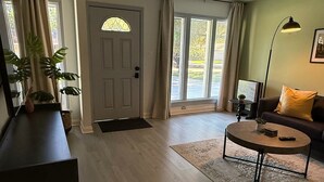 Un salón amplio con suelo de madera, un sofá oscuro, una mesa de centro redonda y un ventanal con cortinas.