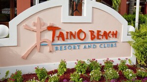 Une enseigne pour le Taino Beach Resort et ses clubs, avec un palmier stylisé et une croix.