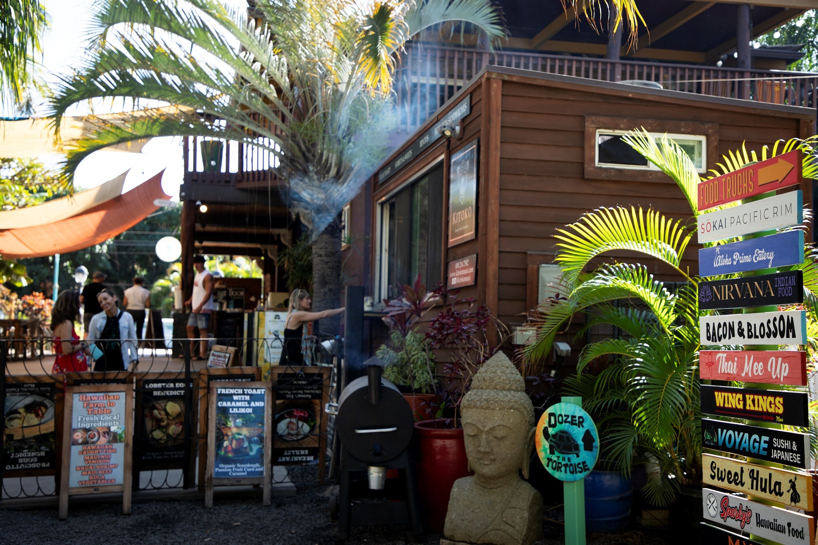 A food truck area with signs for various cuisines and a Buddha statue.