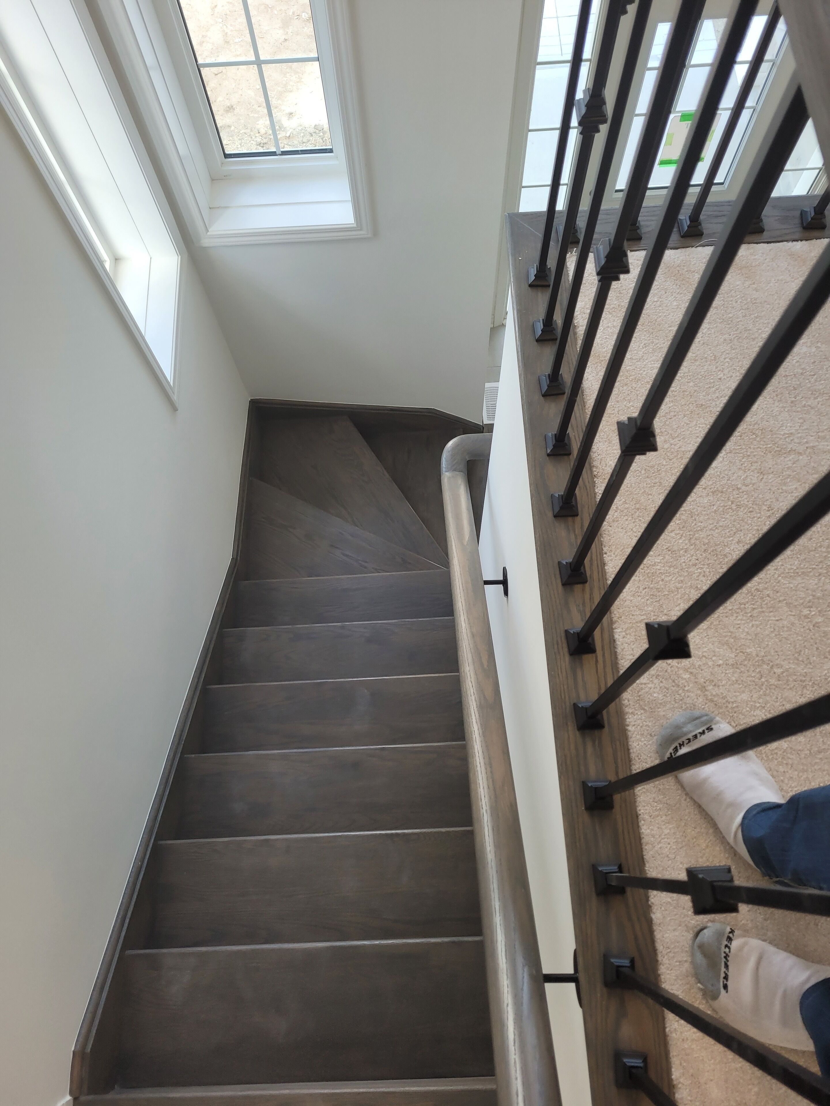 A staircase with a dark wooden finish, white walls, and a metal handrail.