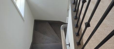 A staircase with a dark wooden finish, white walls, and a metal handrail.