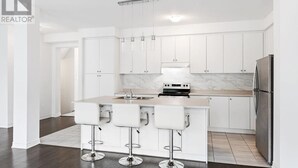 A modern kitchen with white cabinets, a marble backsplash, a stainless steel refrigerator, and a central island with bar stools.