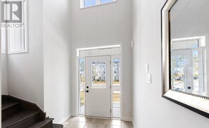A clean, modern hallway with a white door leading outside, a large mirror on the right, and a dark staircase on the left. - Golf course Access, 5mins to Main Beach, Wasaga 500 (Go-Kart, Batting Cage) (Wasaga Beach)