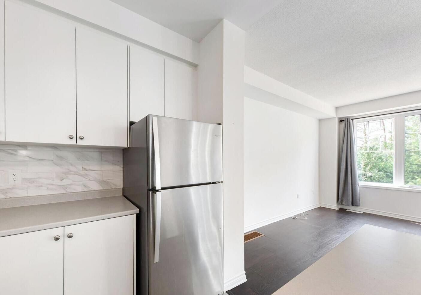 Una cocina moderna con armarios blancos, un refrigerador de acero inoxidable y un ventanal que proporciona luz natural.