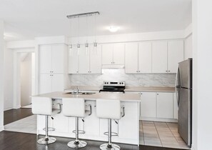 A modern kitchen with white cabinets, a marble backsplash, a stainless steel refrigerator, and a central island with bar stools.